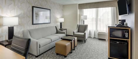 A hotel room with a sofa, two armchairs, a coffee table, a TV, a microwave, and a small refrigerator.