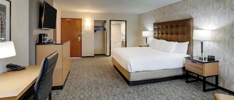 A hotel room with a bed, desk, chair, TV, and a bathroom visible through an open door.