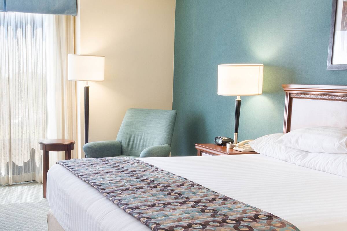 Una habitación de hotel con cama, una silla, un escritorio con lámpara y teléfono.