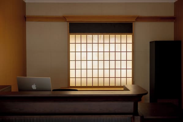 Una stanza con una scrivania in legno, un computer portatile e un tradizionale pannello giapponese shoji.