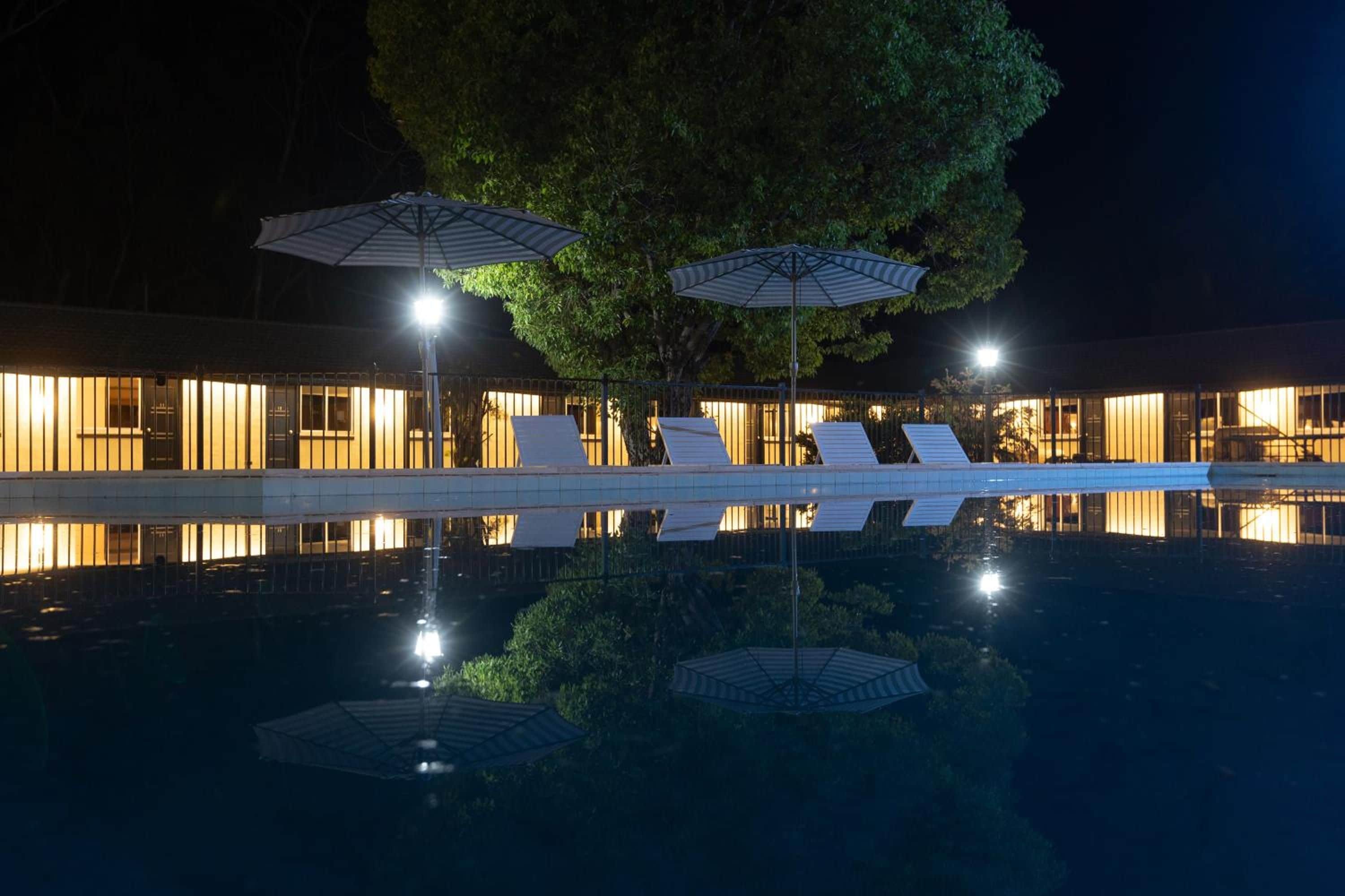 A nighttime view of a hotel with a pool, umbrellas, and lounge chairs.