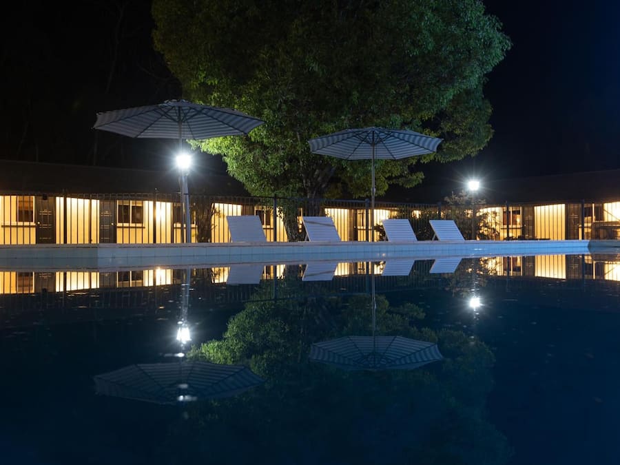 A nighttime view of a hotel with a pool, umbrellas, and lounge chairs.