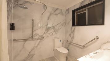A bathroom with a shower, toilet, and sink, featuring marble walls and handrails.