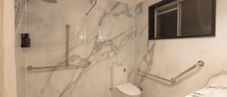 A bathroom with a shower, toilet, and sink, featuring marble walls and handrails.