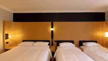Une chambre d’hôtel avec deux lits simples, une tête de lit en bois et un luminaire fixé au mur.