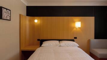 A hotel room with a bed, a nightstand, a chair, and two wall-mounted lights.