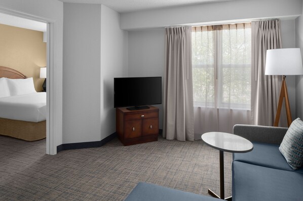 Una habitación de hotel con una cama, un televisor sobre un mueble de madera, un sofá, una mesita y una lámpara.