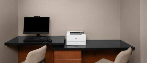 Una oficina pequeña con un escritorio, dos sillas, un monitor de computadora e impresora.