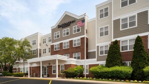 A multi-story hotel with a prominent American flag, a covered entrance, and a brick facade. - Residence Inn by Marriott Long Island Holtsville (Holtsville)