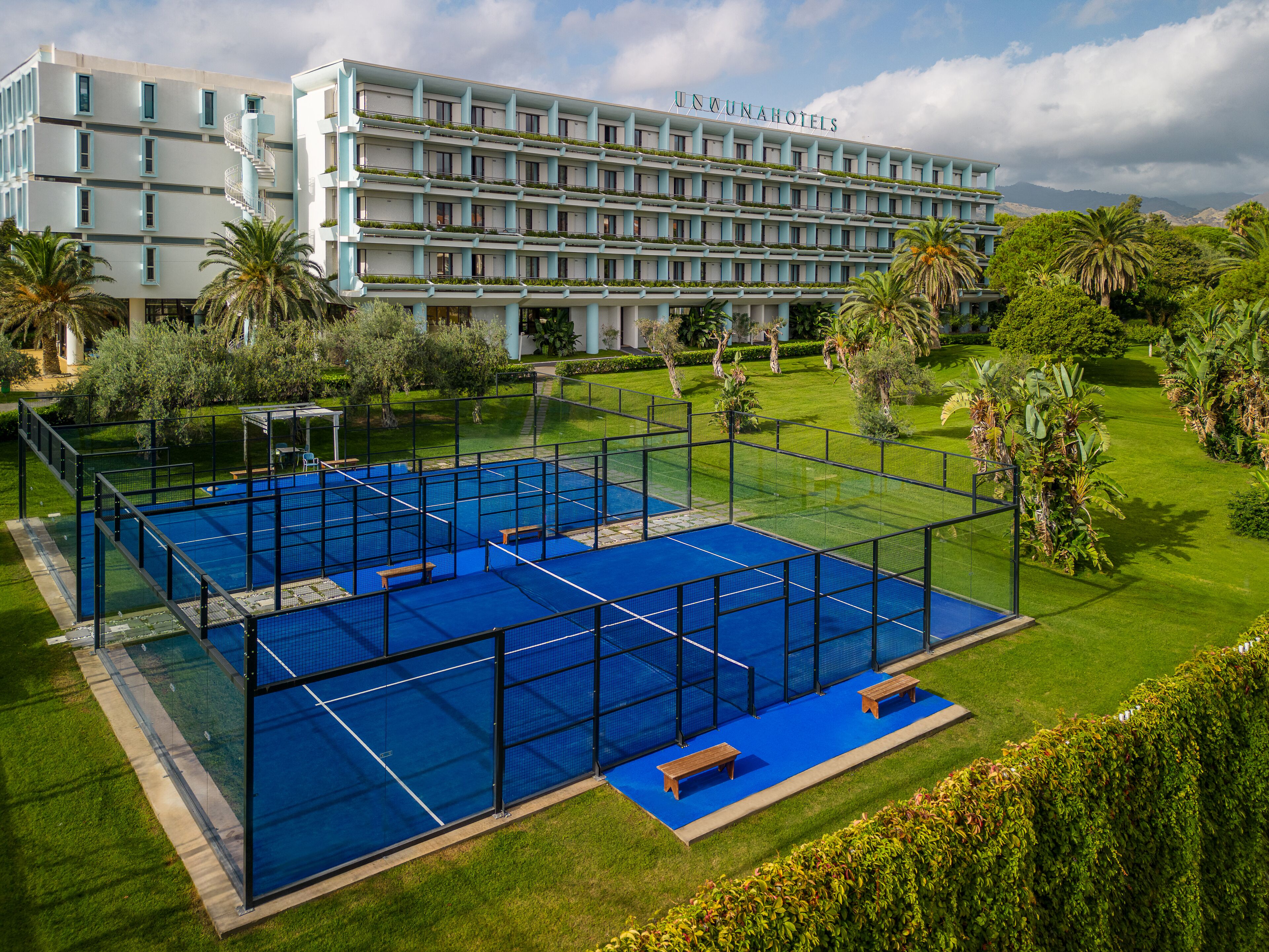 Et hotel med en stor udendørs tennisbane, frodigt grønt område og en flerlænget bygning med altaner.