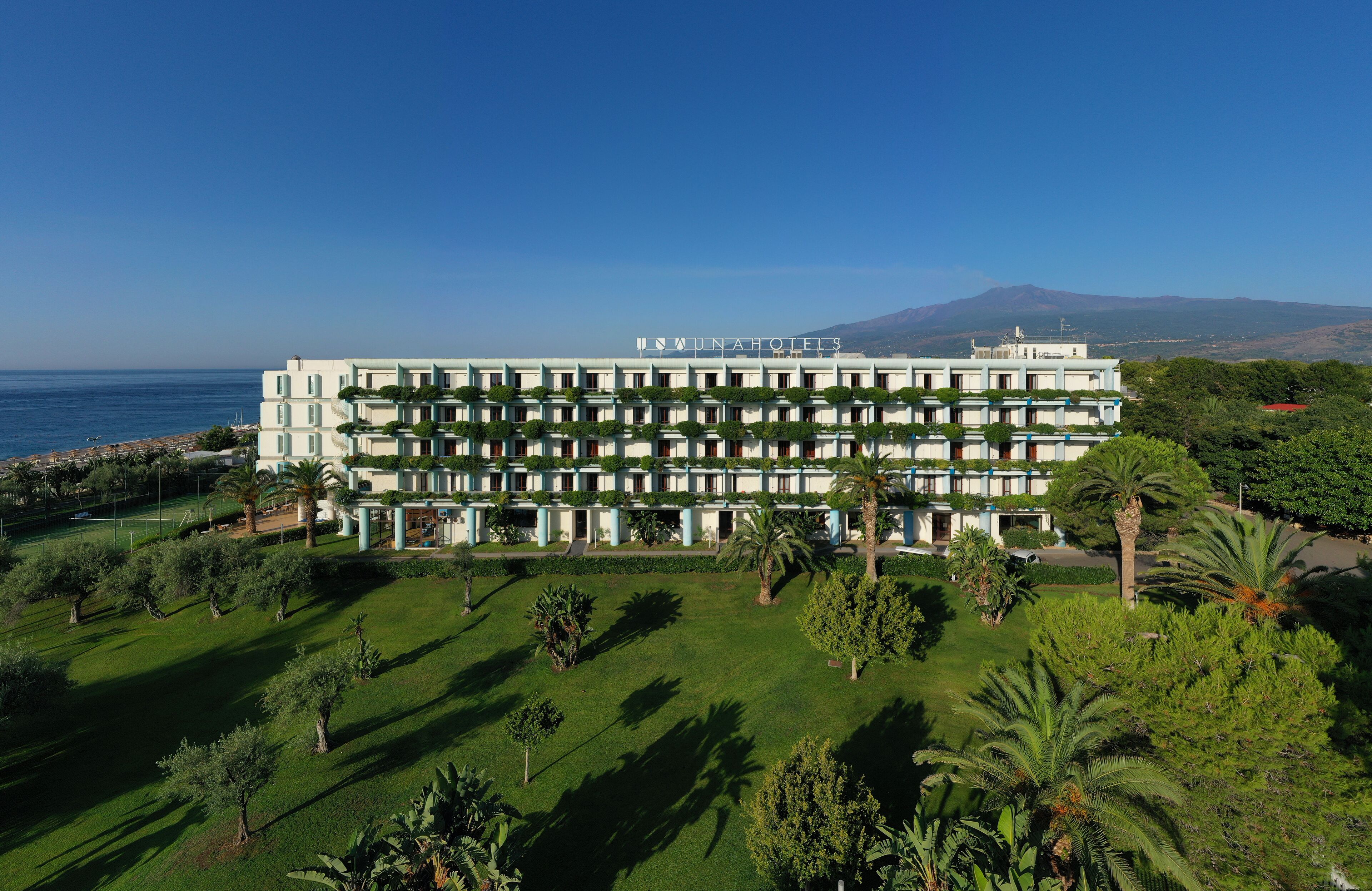 Un hôtel à plusieurs étages, doté d’une façade symétrique, d’une pelouse bien entretenue et offrant une vue sur la mer.