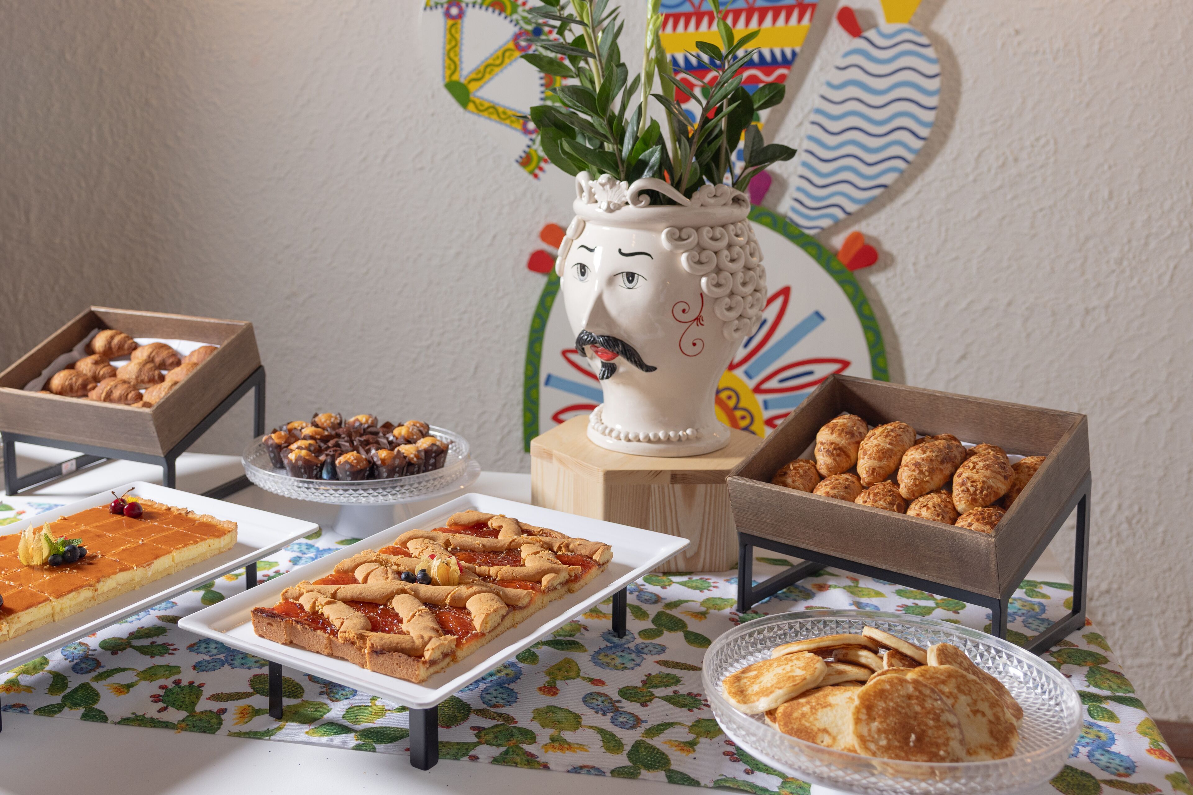 Een tafel met diverse desserts en gebak, waaronder een taart met een gezicht ontwerp, gepresenteerd op een tafel met een bloemrijk tafelkleed.
