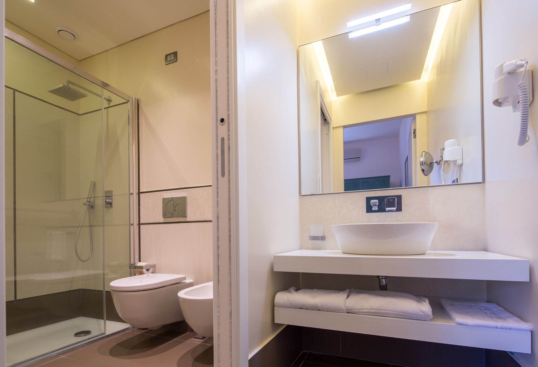 Ein modernes Badezimmer mit einer gläsernen Duschkabine, einer weißen Toilette, einem großen Spiegel und einem weißen Waschbecken mit Becken.