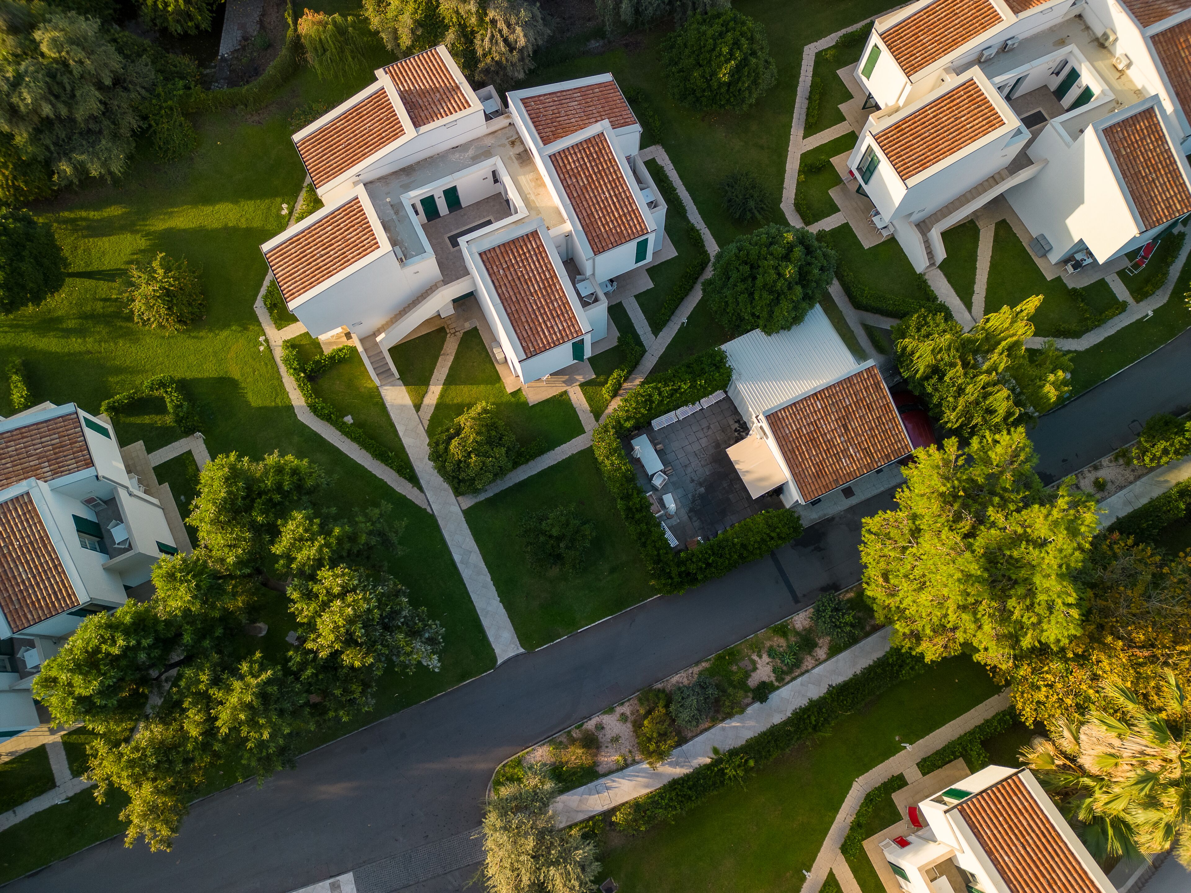 An aerial view of a residential area with multiple houses featuring red-tiled roofs and white exteriors, surrounded by well-maintained lawns and trees.