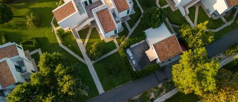 An aerial view of a residential area with multiple houses featuring red-tiled roofs and white exteriors, surrounded by well-maintained lawns and trees.
