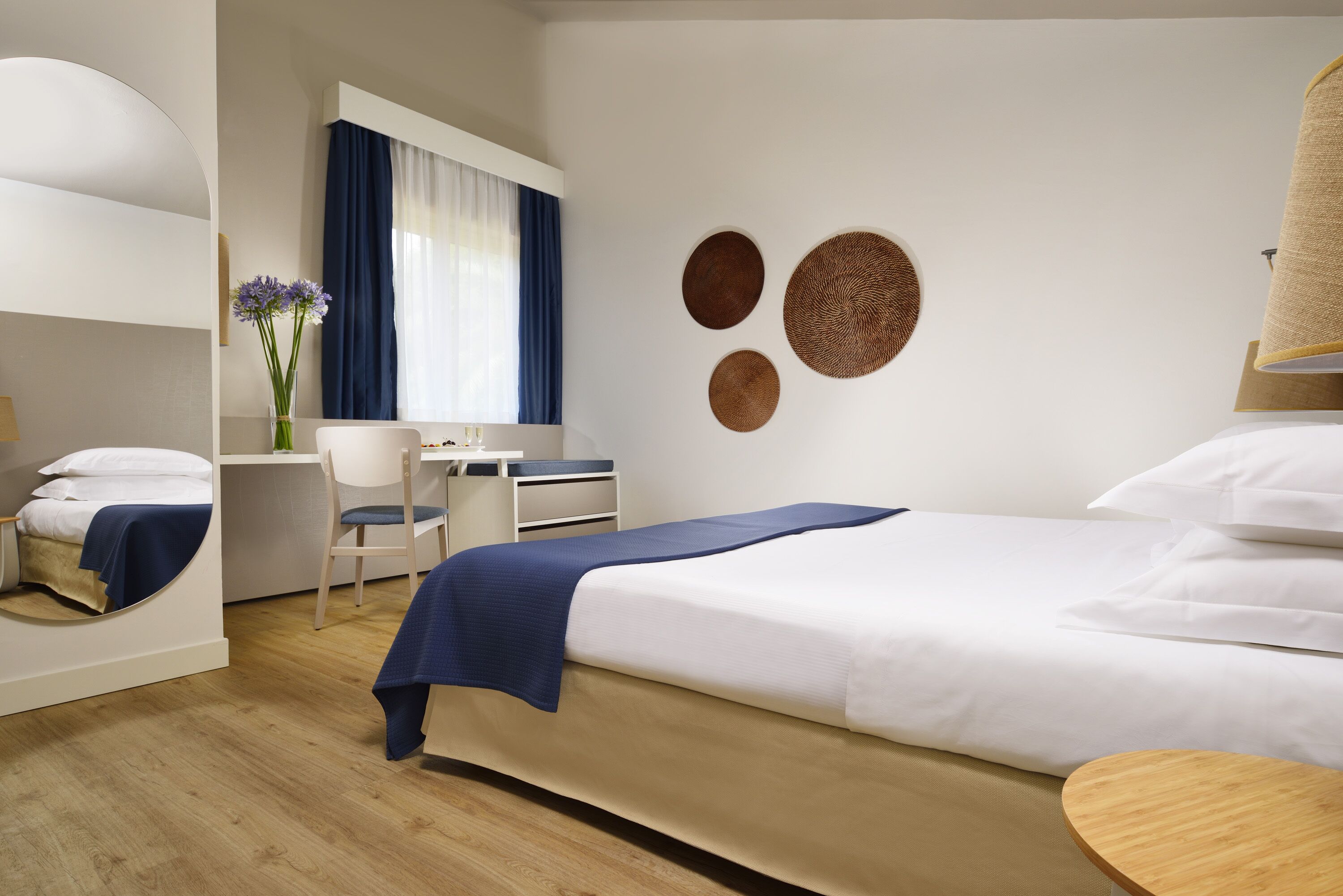 Quarto de hotel com cama, escrivaninha, cadeira e espelho.