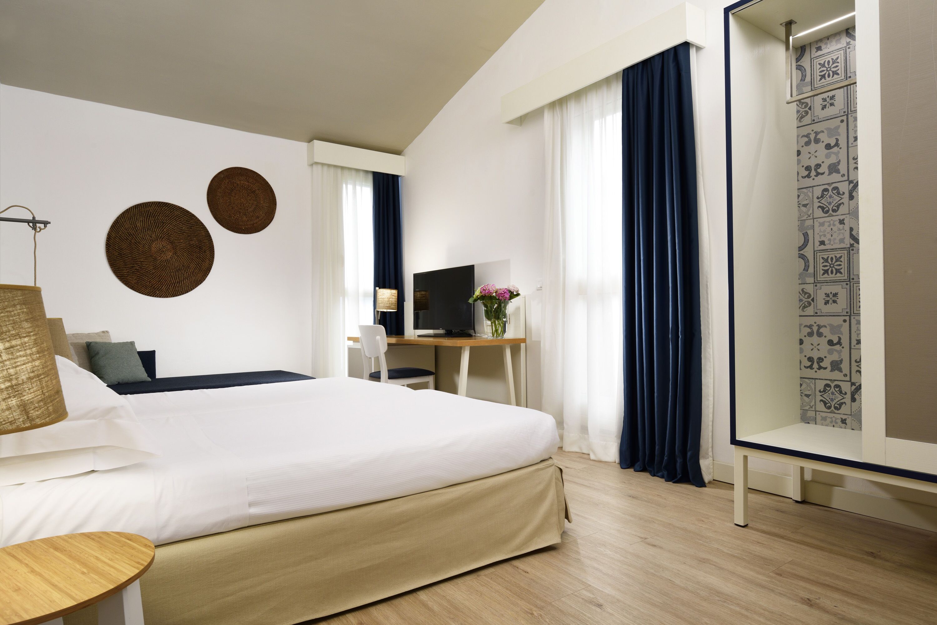 Una habitación de hotel moderna con una cama grande, un escritorio, una silla, un televisor y arte decorativo en la pared.