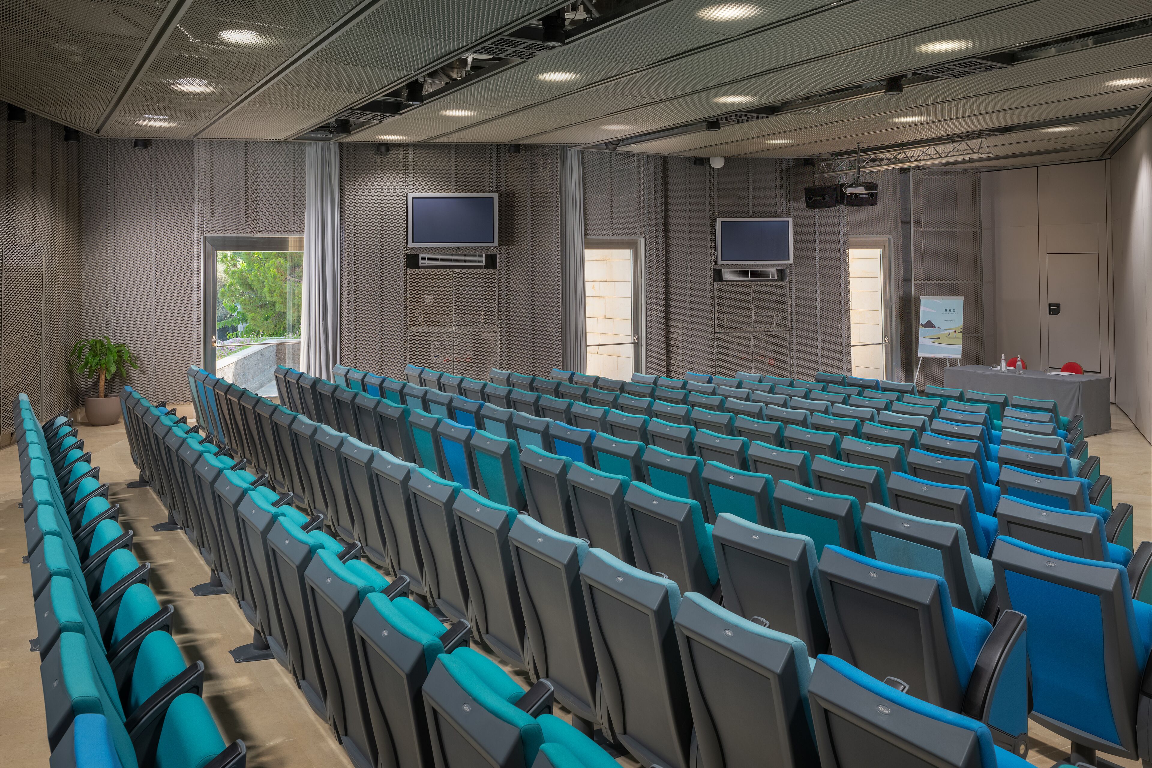 A conference room with rows of blue and gray chairs, a large screen, and a projector.