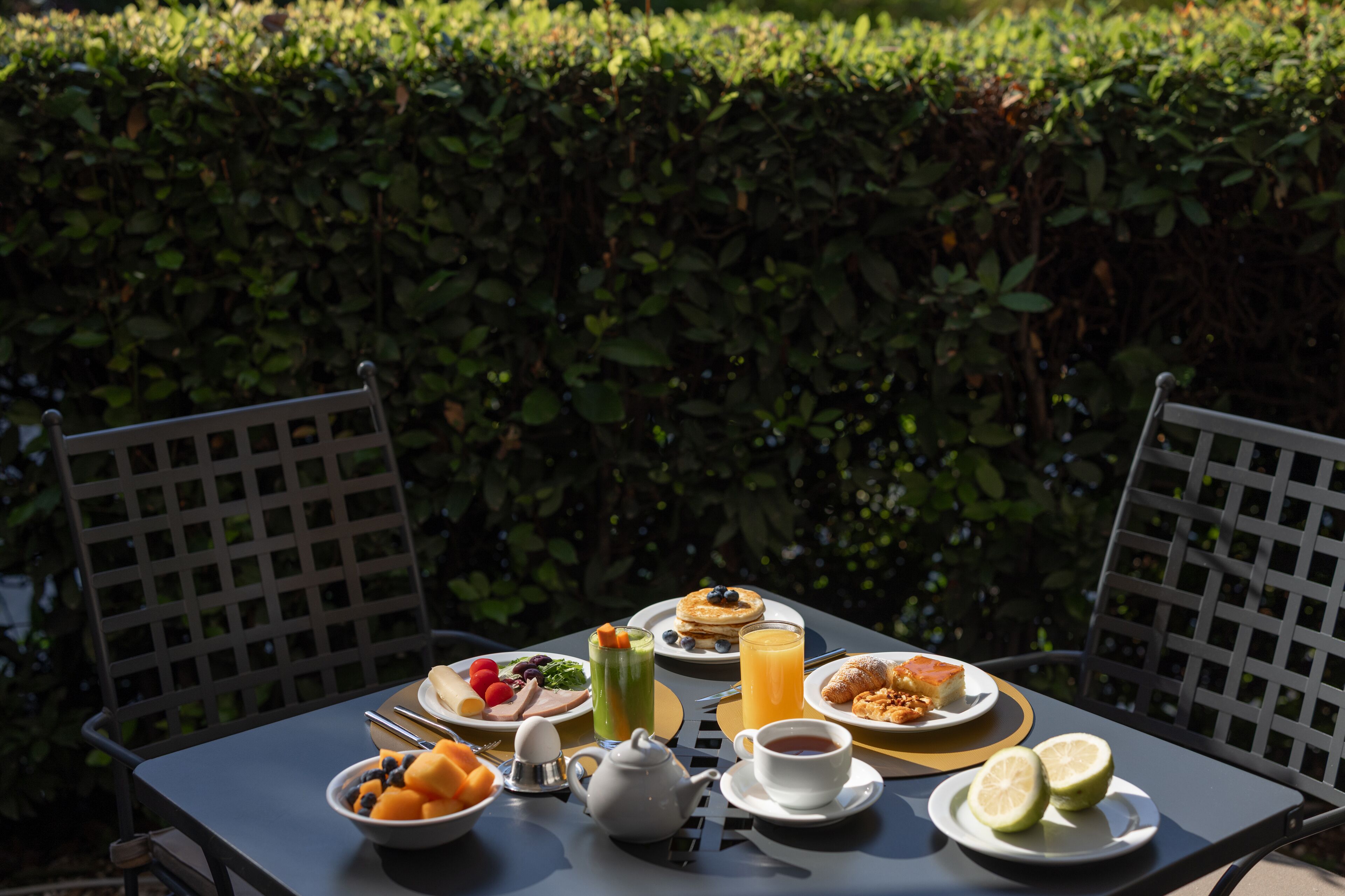 A table set outdoors with breakfast items including pancakes, fruit, and juice.