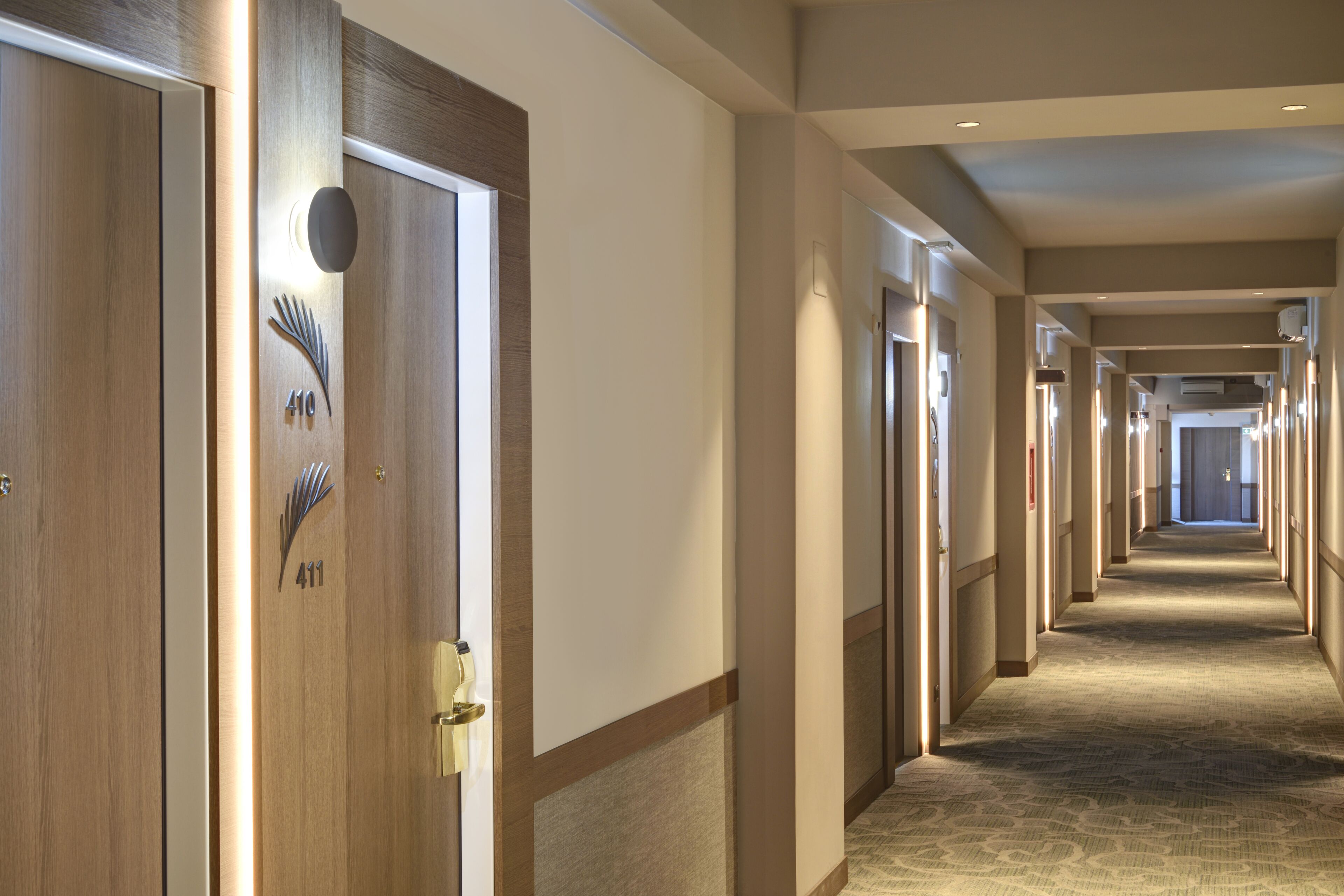 Um corredor de hotel com portas numeradas 410 e 411, chão coberto de carpete e um longo vão com portas de ambos os lados.