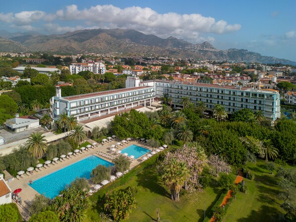 Un hotel con una piscina amplia, exuberante vegetación y vistas a montañas.