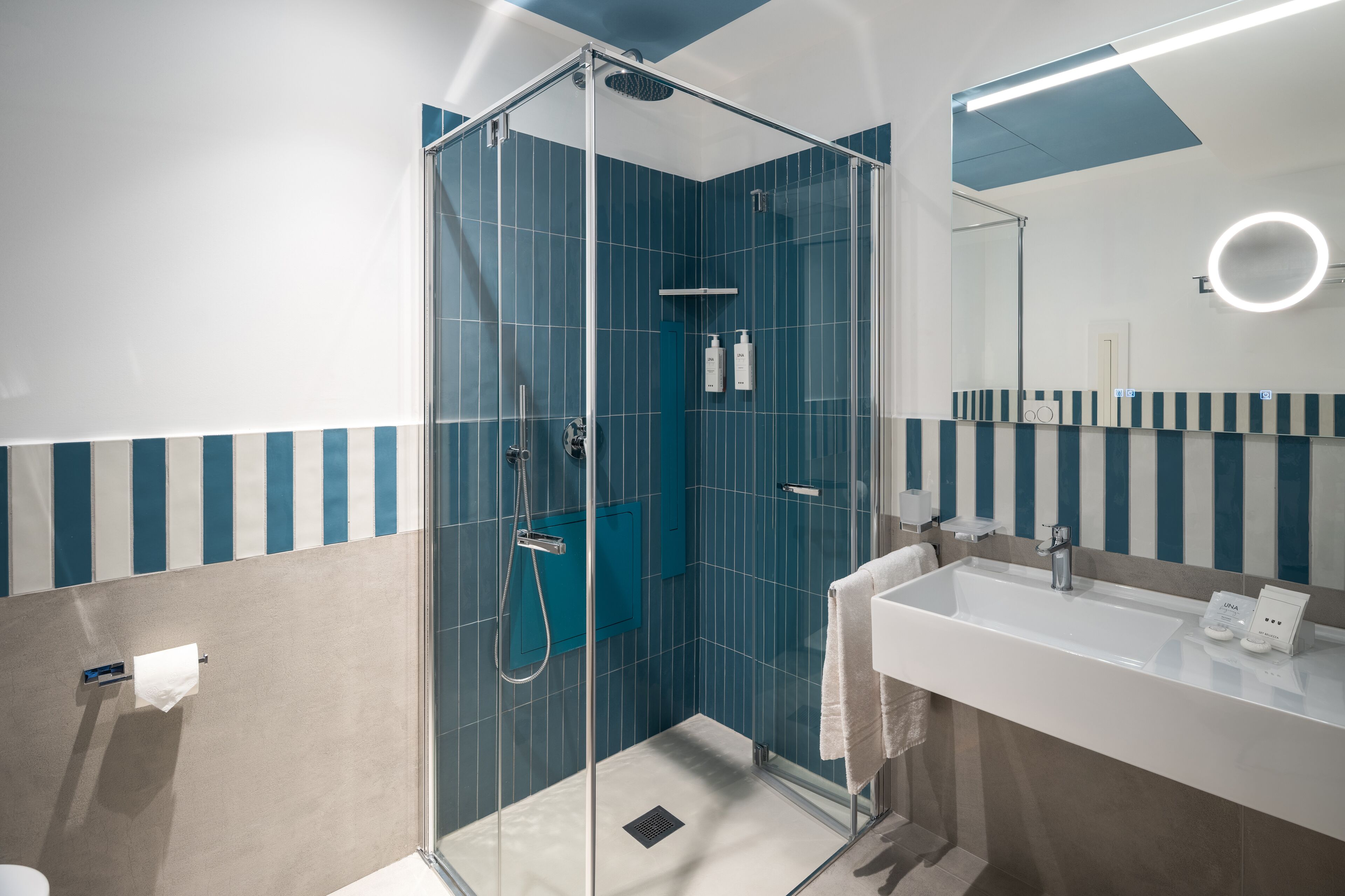 A modern bathroom with a glass-enclosed shower, a white sink, and a mirror with a circular light.