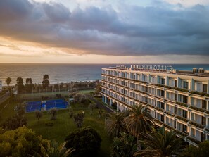 Un hotel con varios balcones, una cancha de tenis y vista al océano.