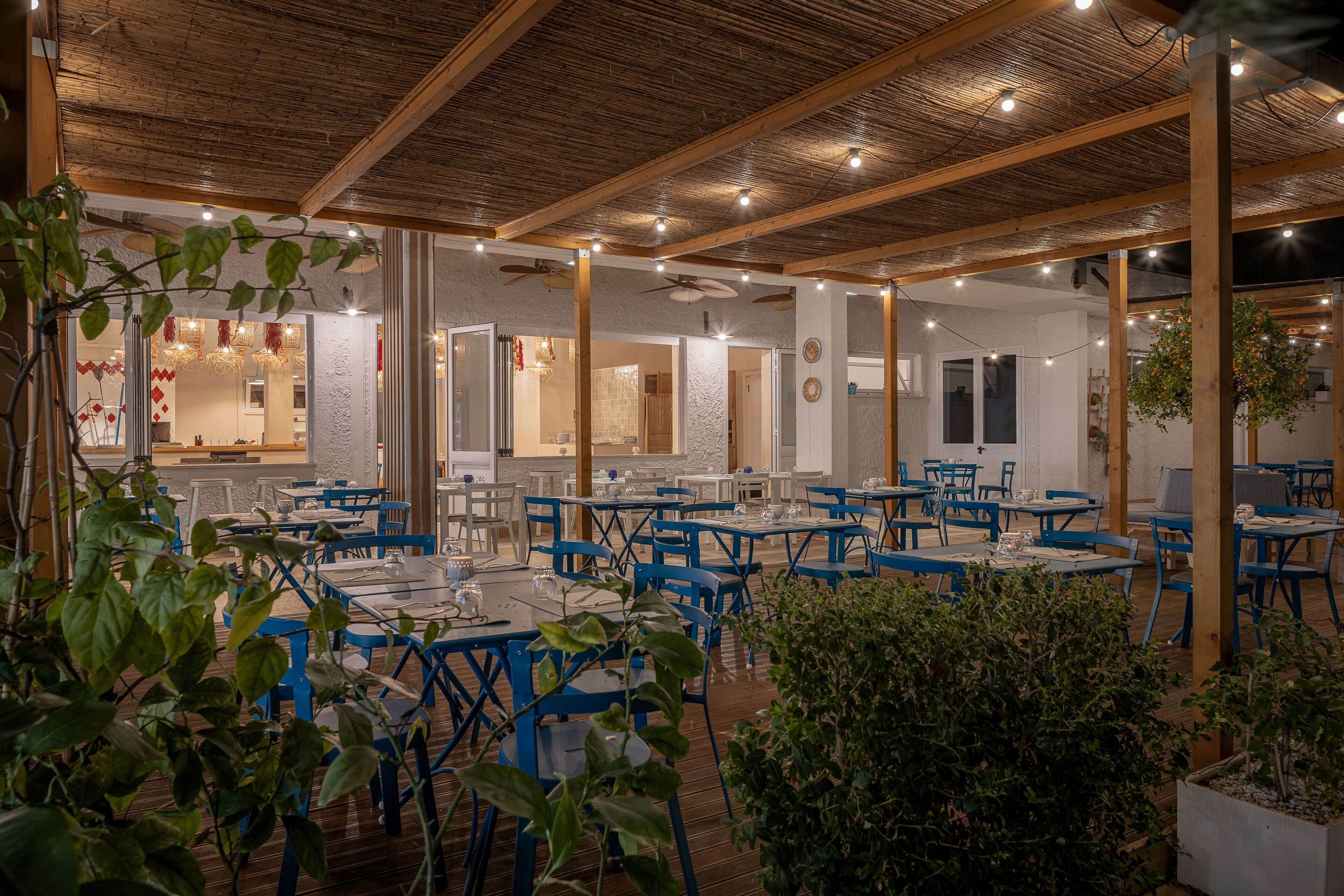 Un'area pranzo interna con tavoli e sedie blu, travi di legno e luci a catena.