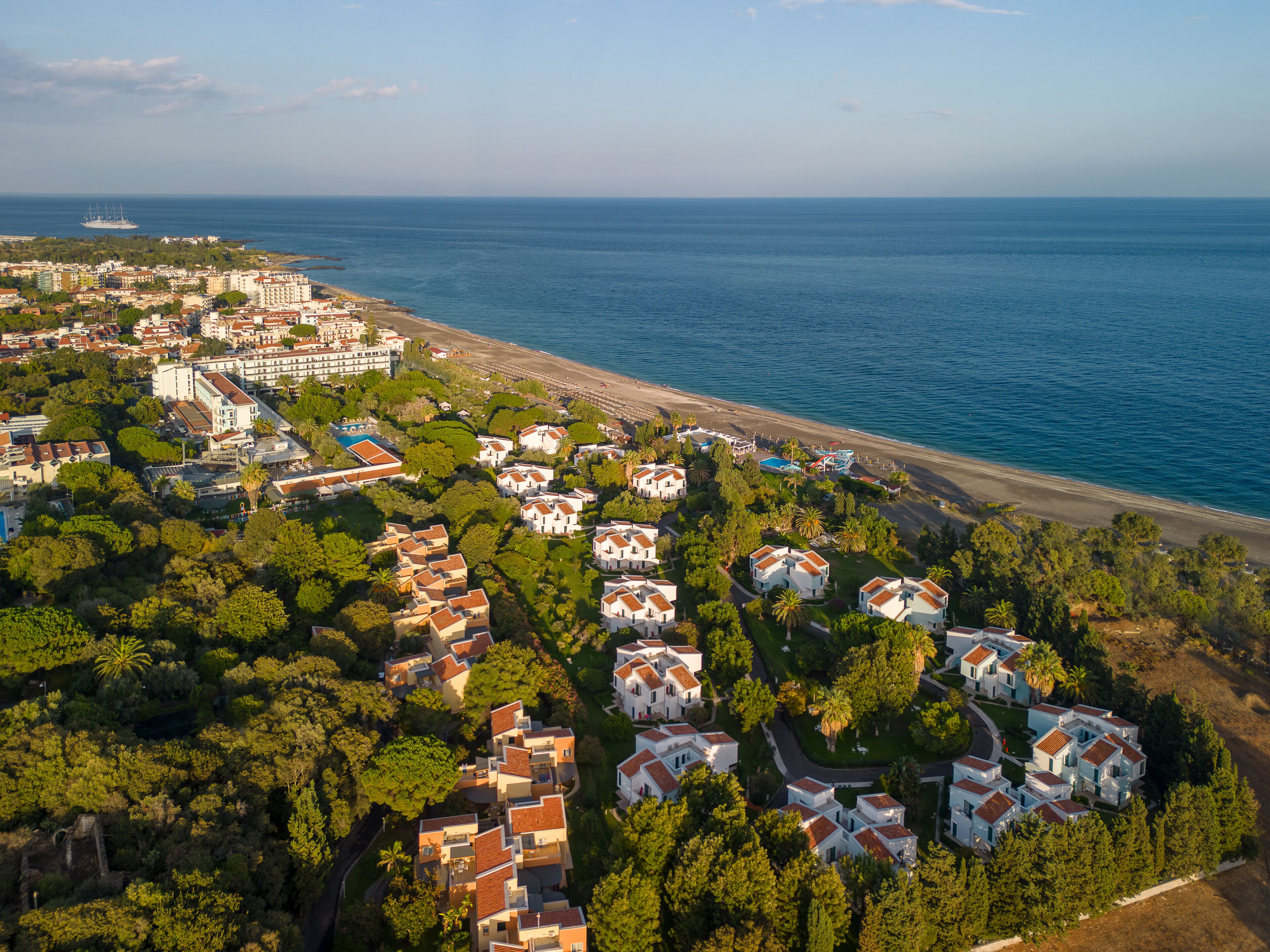 Vista aérea de una zona residencial costera con casas, una playa y un yate a lo lejos.