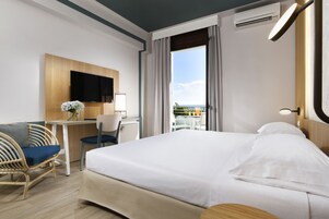 Quarto de hotel com cama, escrivaninha, cadeira, televisão e vista para o exterior.