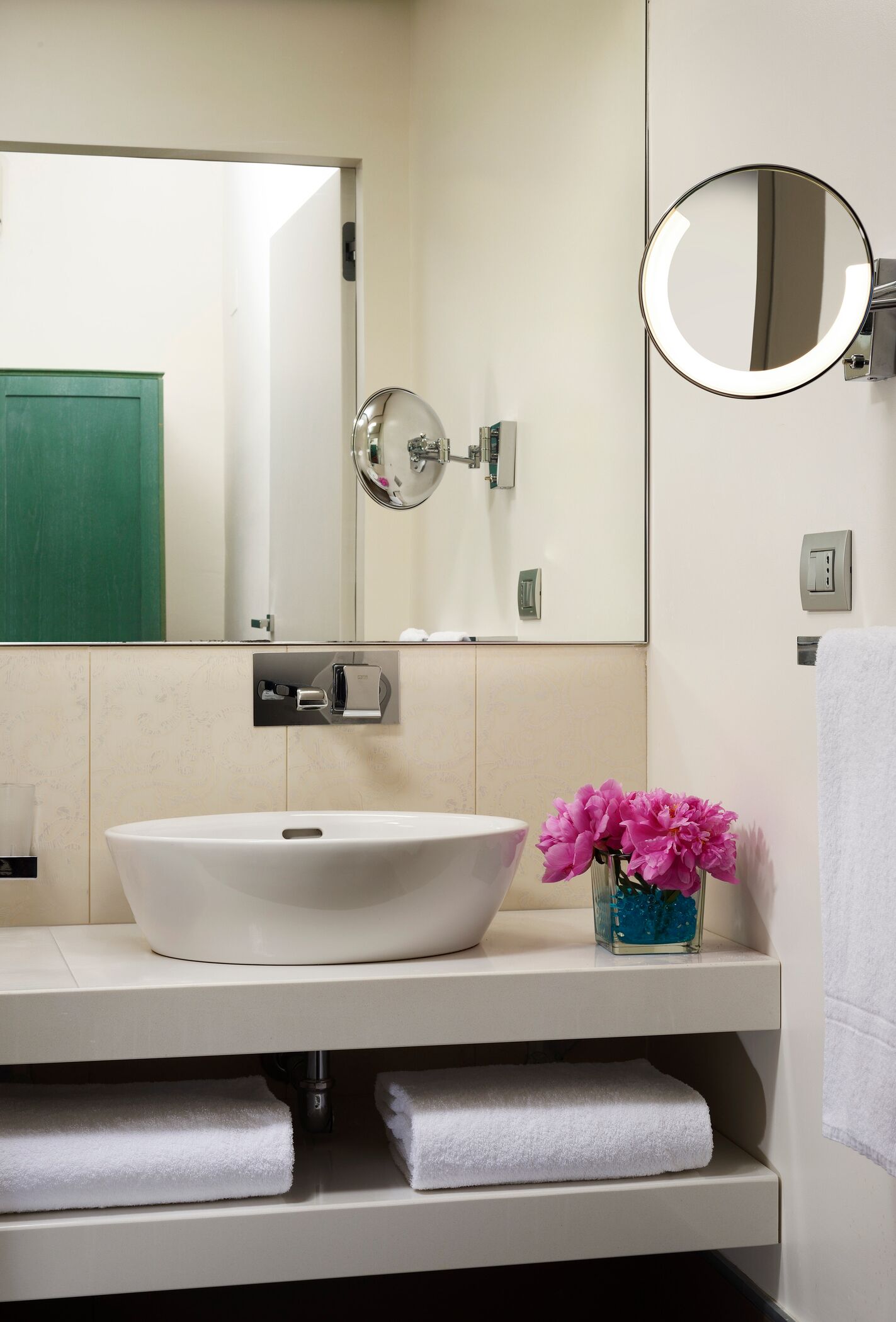 A bathroom with a white sink, a mirror, a green door, and a vase with pink flowers.