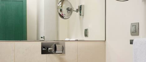 A bathroom with a white sink, a mirror, a green door, and a vase with pink flowers.