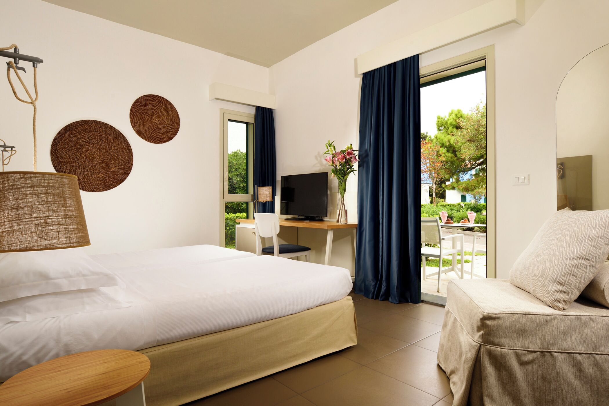 A hotel room with a bed, a desk with a computer, a chair, and a view of the outdoors.