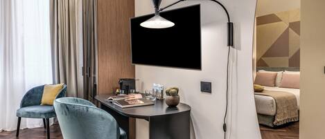 A modern room with a dark wooden desk, a blue chair, a mounted TV, and a bed with a geometric-patterned headboard.