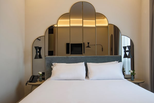 A hotel room with a large bed, a bedside table with a lamp, a phone, and a vase with flowers.