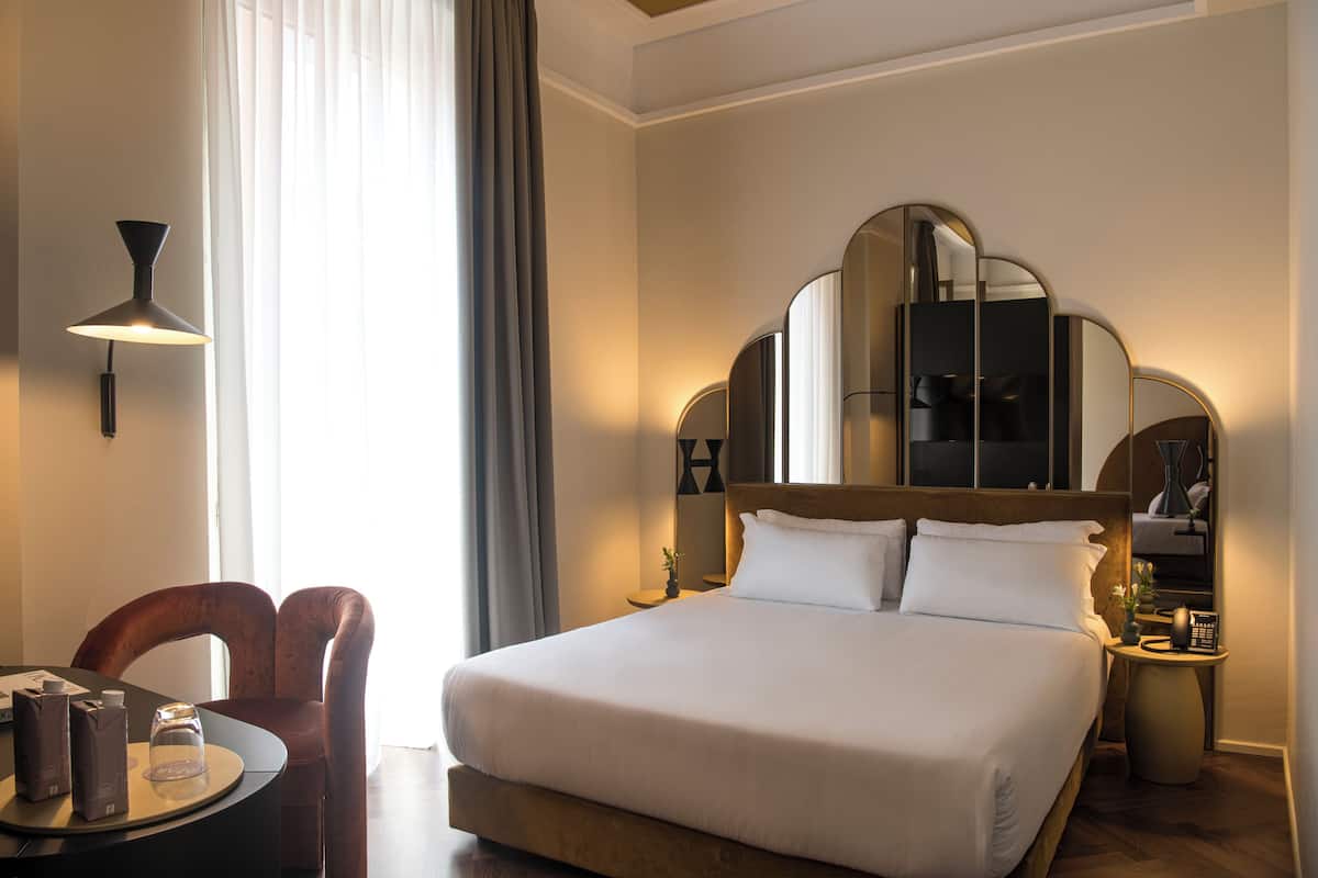 Habitació d'hotel amb un llit gran, un escriptori amb una cadira, una làmpada i un mirall.