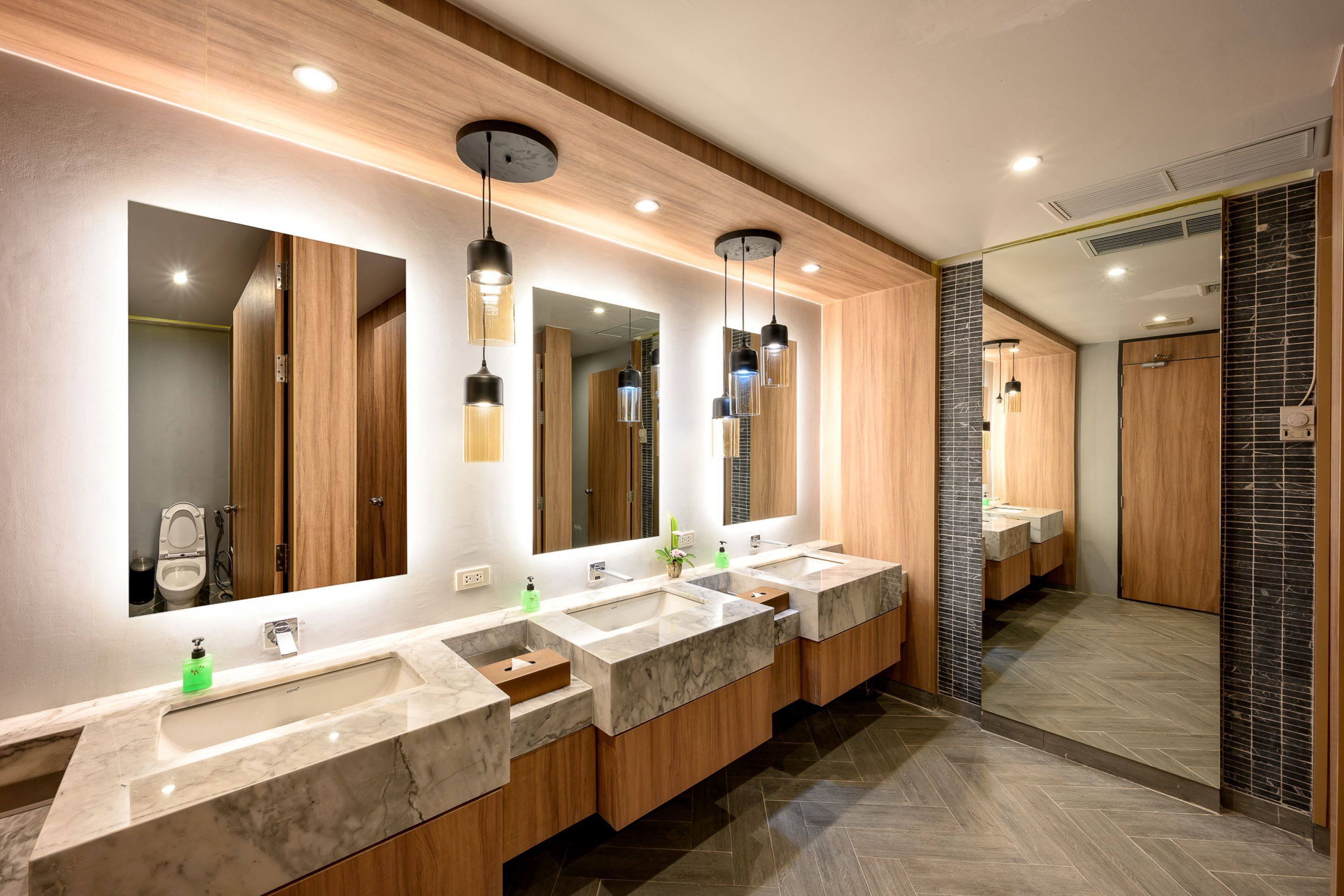 A modern bathroom with three sinks, wooden cabinets, and large mirrors.