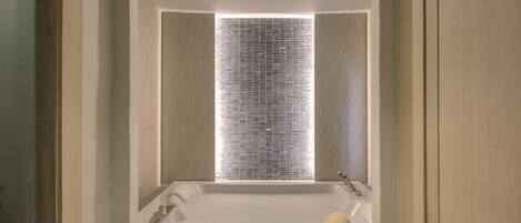 A modern bathroom with a large bathtub, a shower area, and a window with blinds.