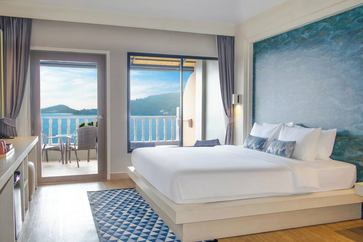 A hotel room with a large bed, a desk, a chair, and a view of the sea.
