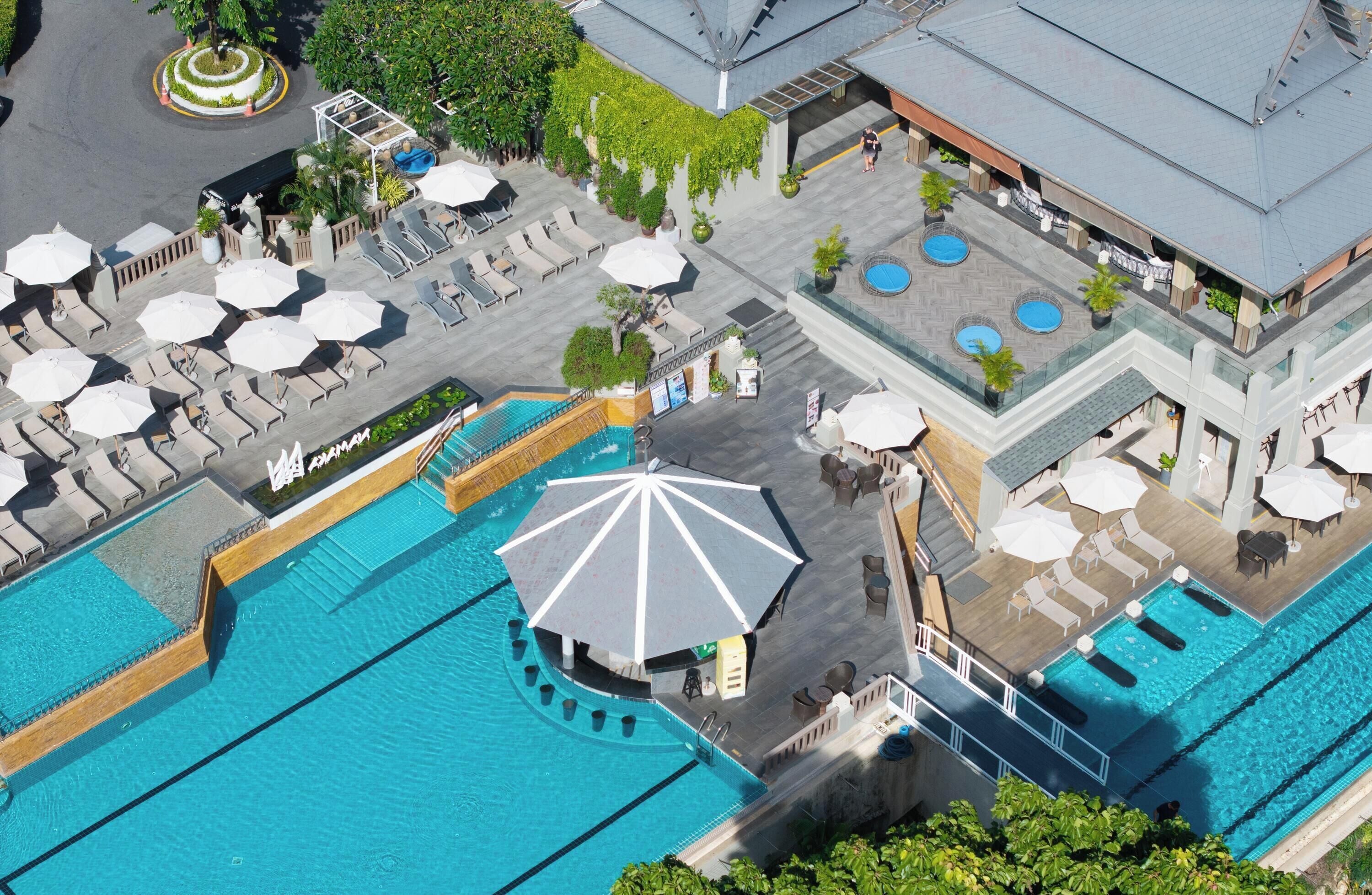 A rooftop pool area with multiple lounge chairs and umbrellas, surrounded by a pool with a central circular seating area.