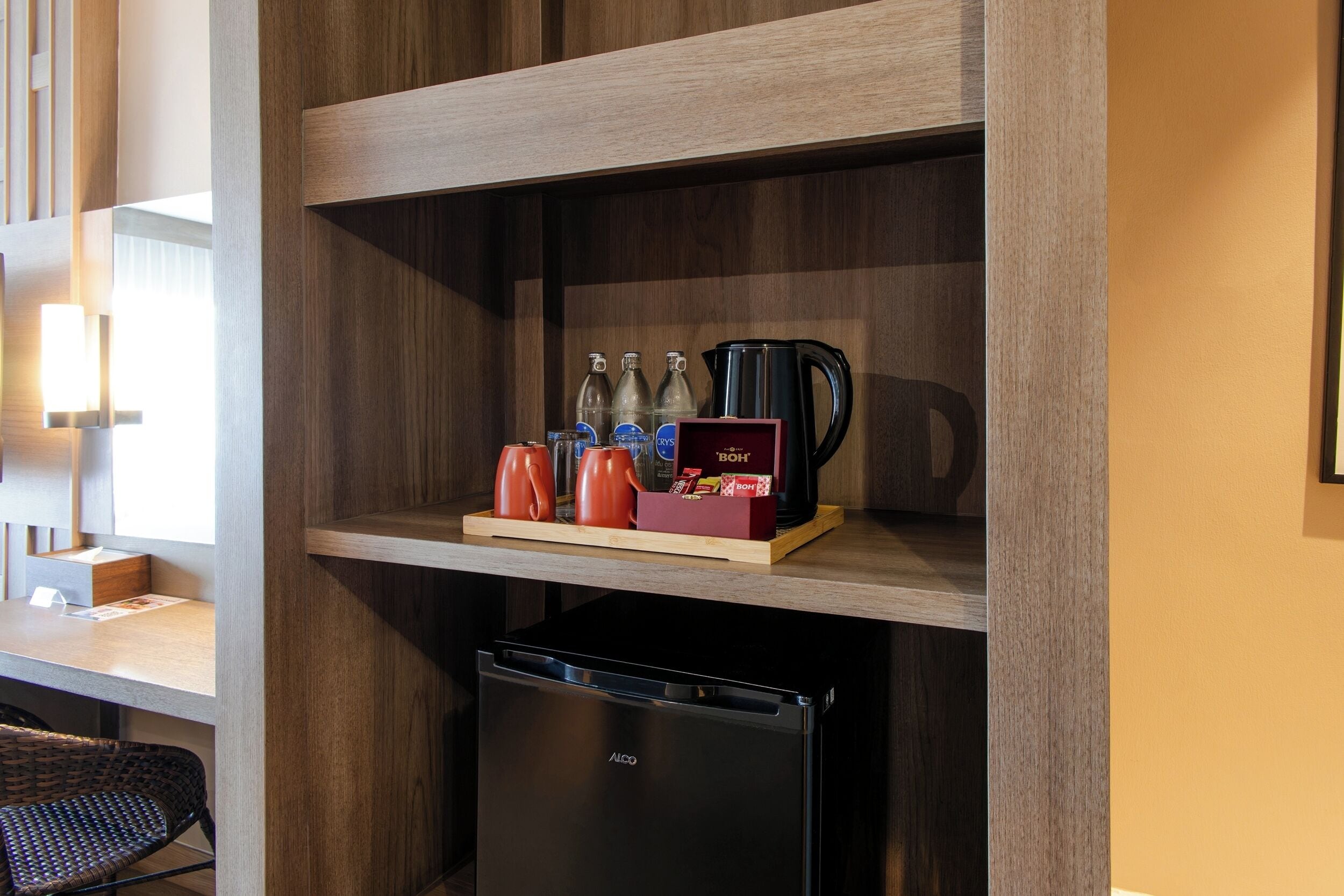 Une petite cuisine équipée d’un réfrigérateur noir, d’une étagère en bois où sont rangés les ustensiles de cuisine et d’une machine à café.