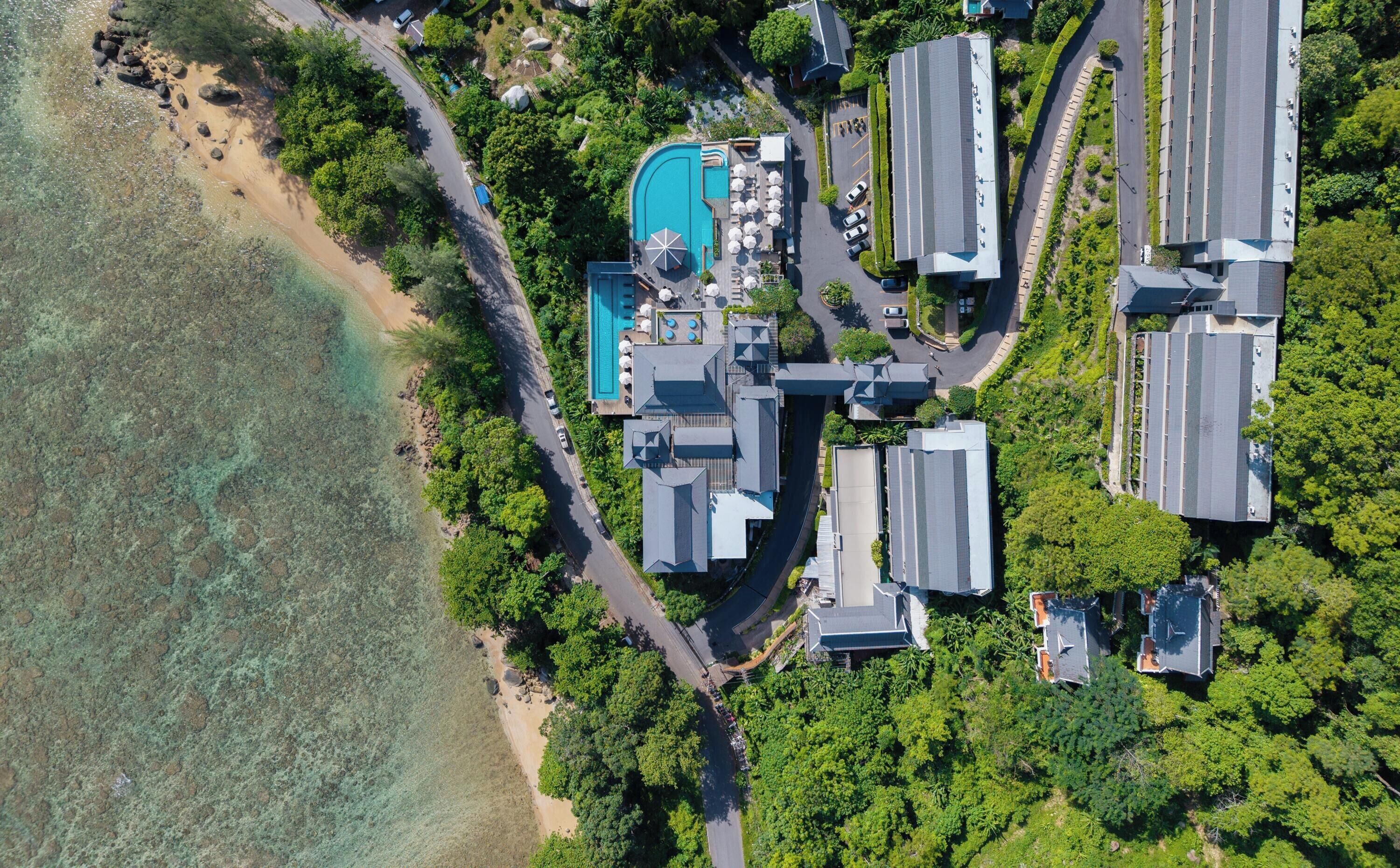 An aerial view of a resort with a swimming pool, multiple buildings, and a beach.