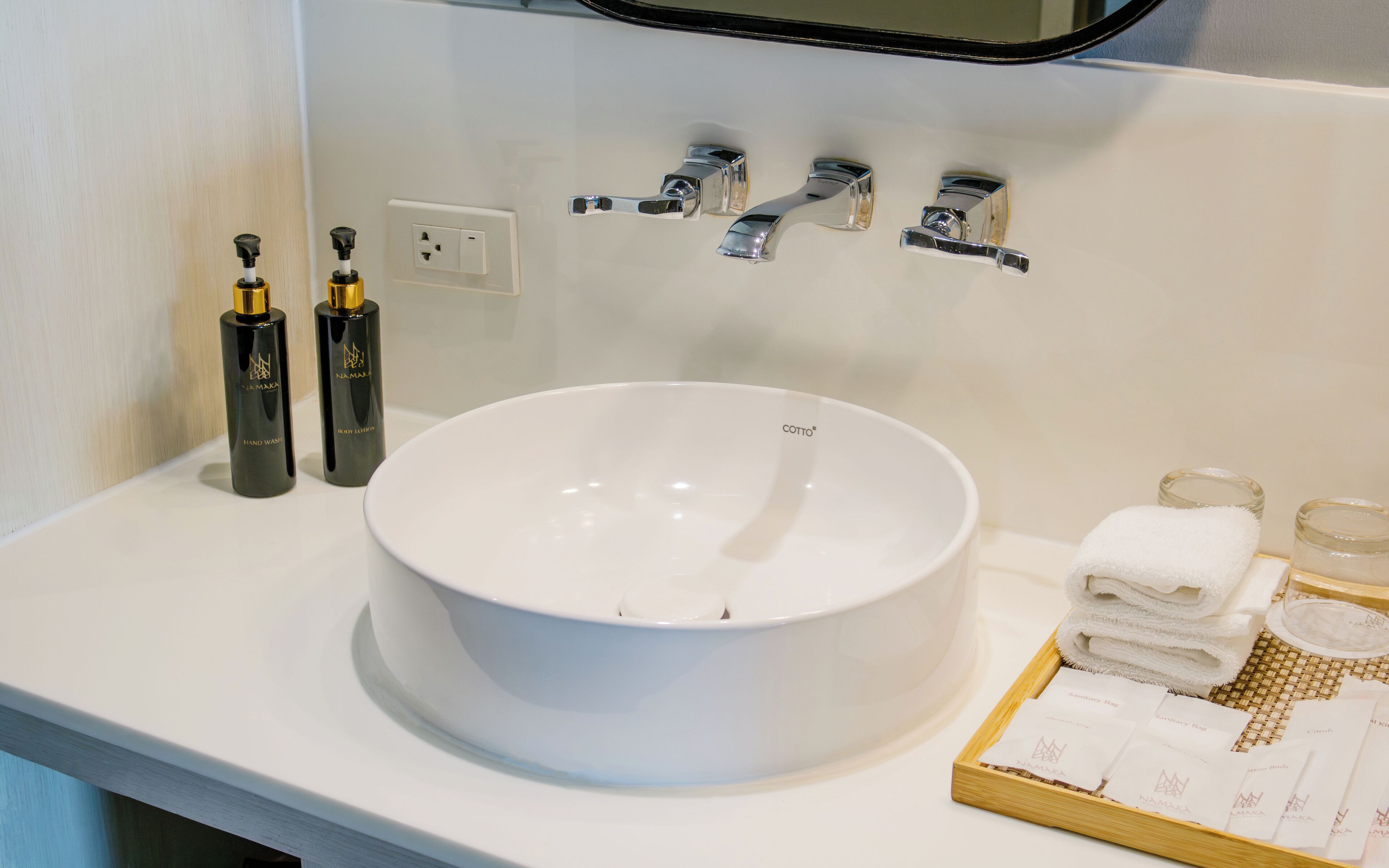 A bathroom with a white sink, two hand soap bottles, a mirror, and a tray with towels and a glass.