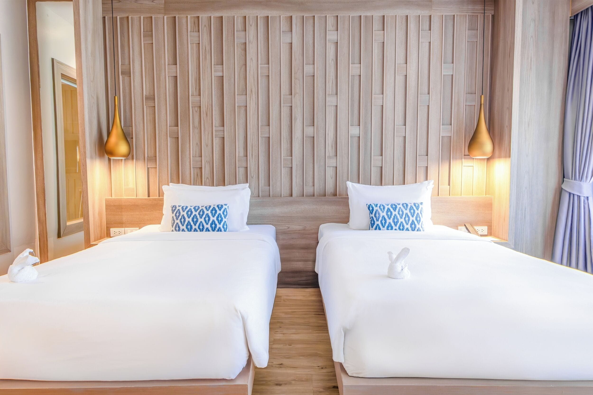 Une chambre d’hôtel avec deux lits, un lambris en bois sur le mur et des luminaires suspendus.