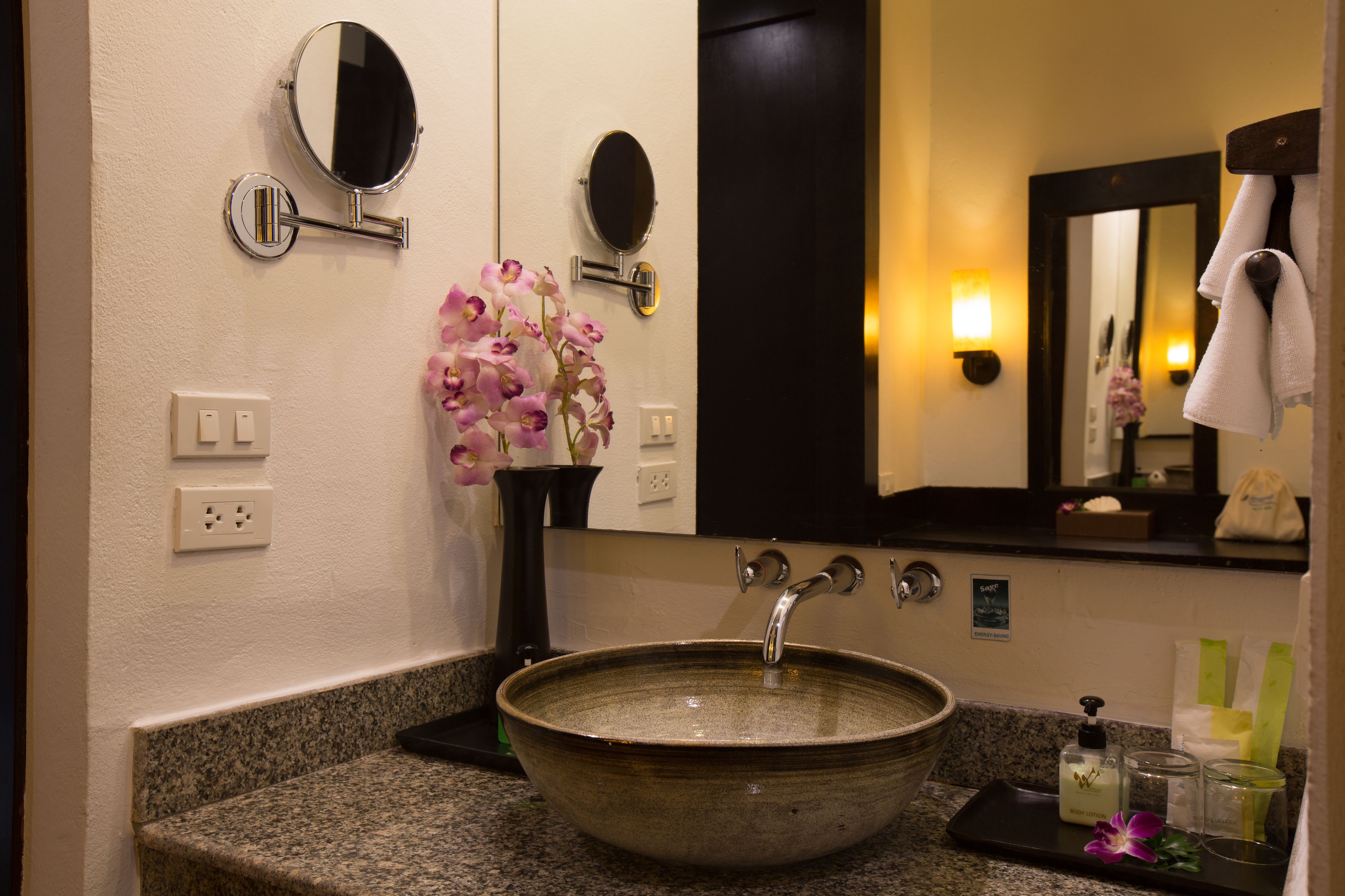 Un baño con un lavamanos de cerámica grande, un espejo y un florero con flores.