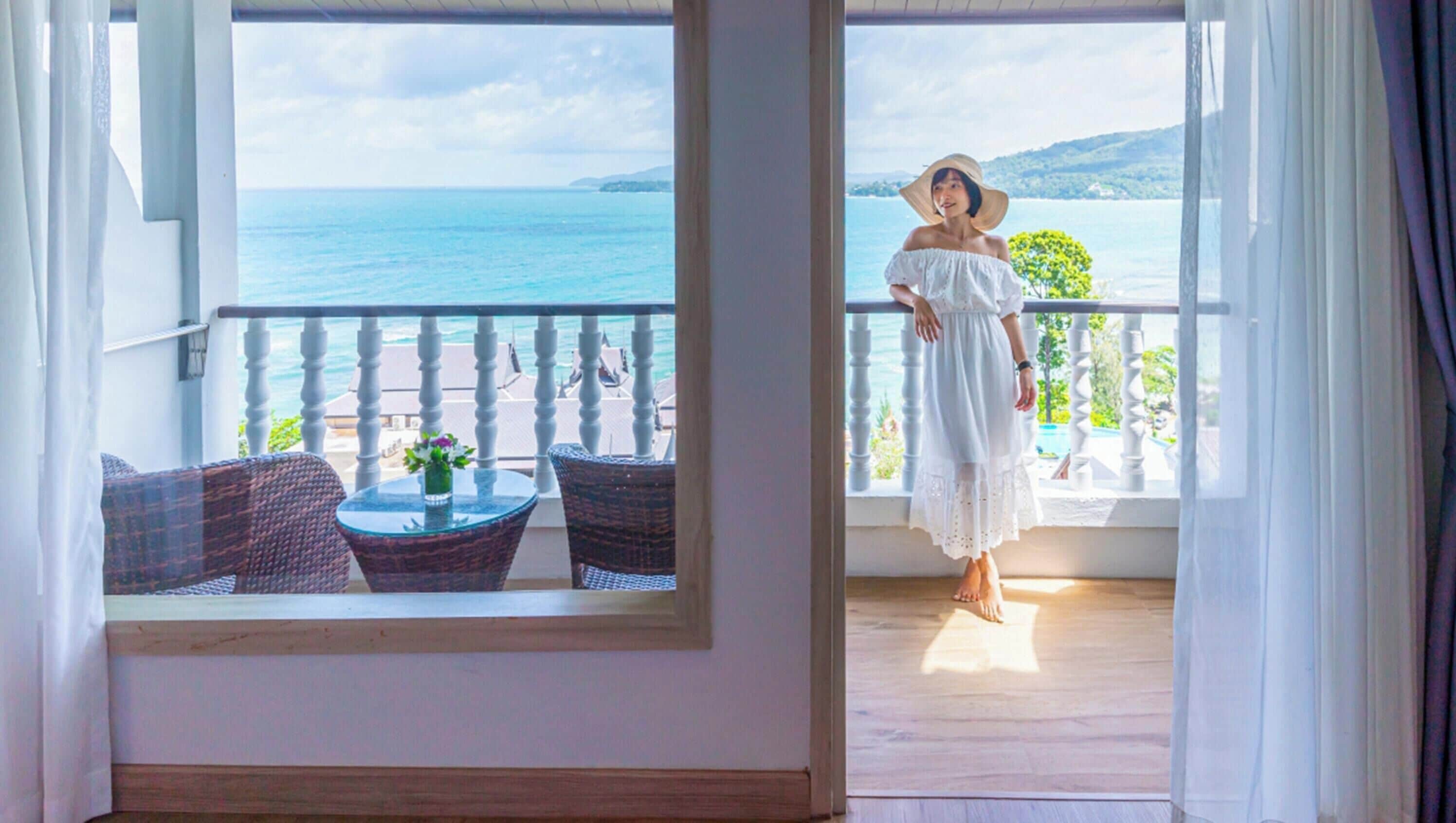 A balcony with wicker furniture and a table, overlooking a body of water and greenery.