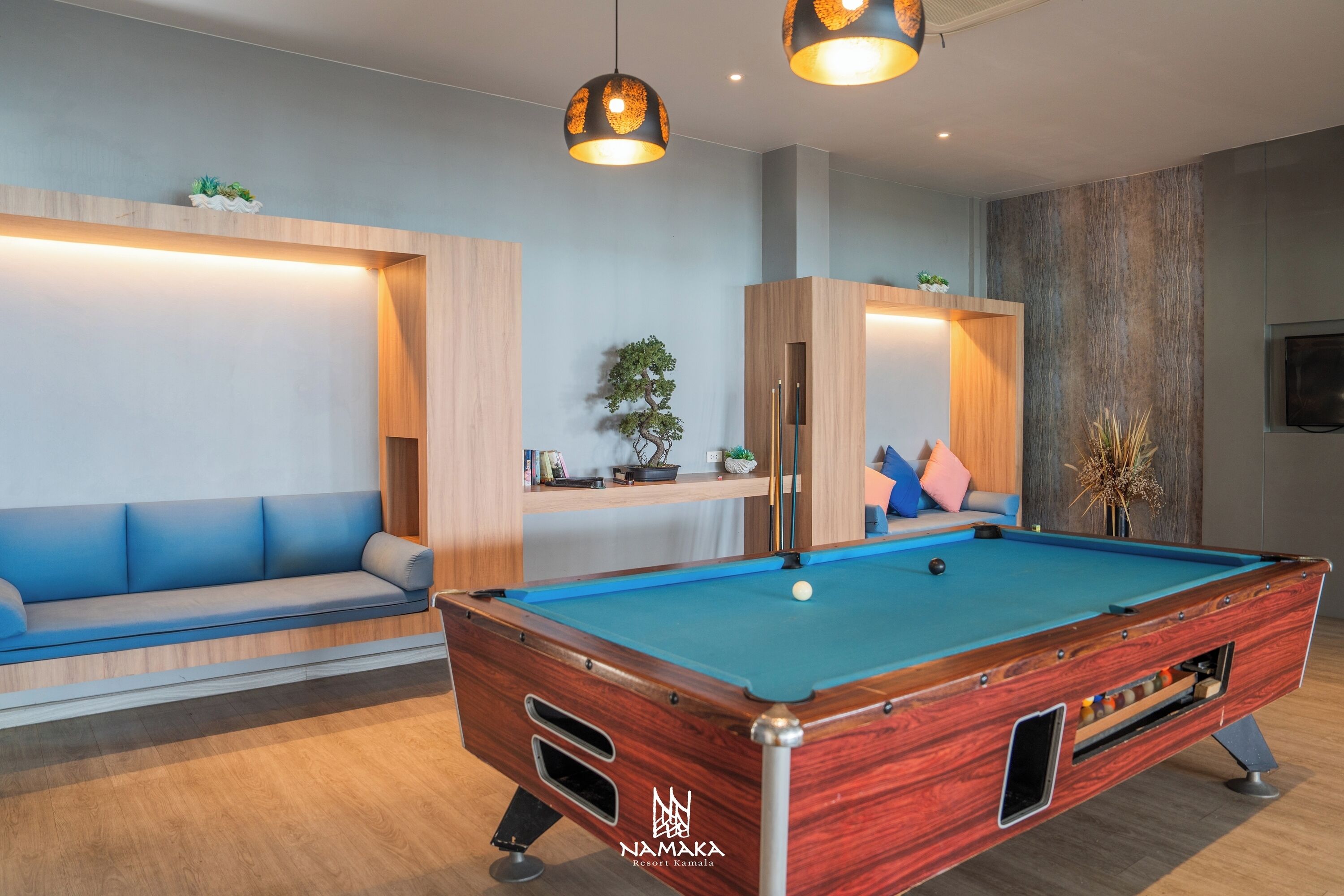 A pool table with a wooden finish, a blue cushioned sofa, and two pendant lights.