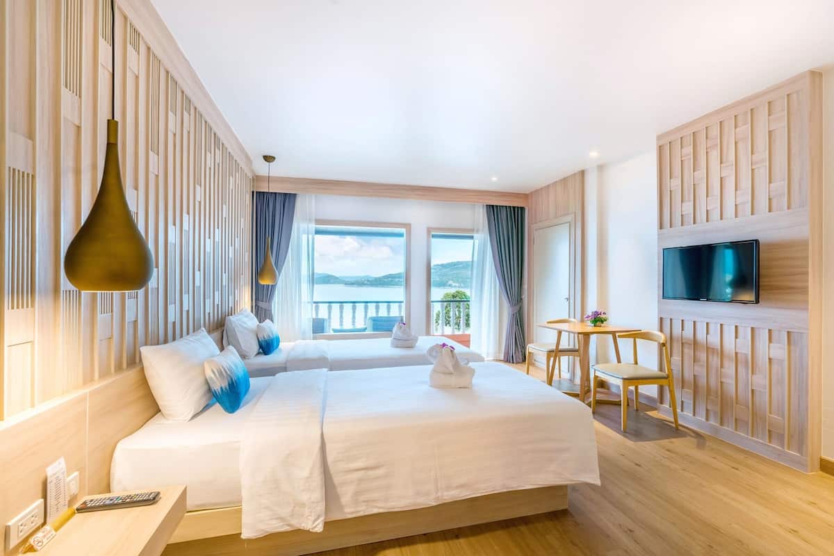 A hotel room with a large bed, a TV mounted on the wall, and a balcony with a view.
