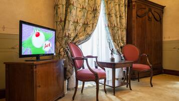 A room with a television on a wooden cabinet, two red upholstered chairs, a wooden table, and a large wooden wardrobe.