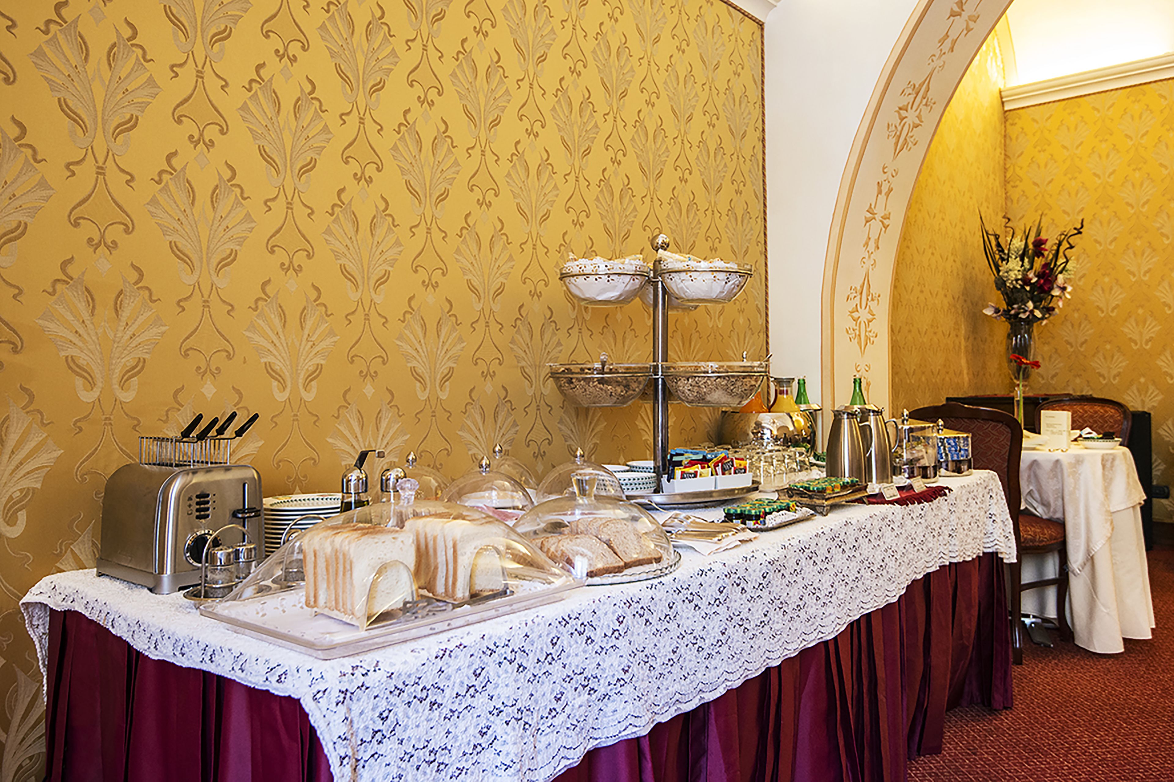 A buffet setup with various food items and a coffee station, set against a patterned wallpaper background.